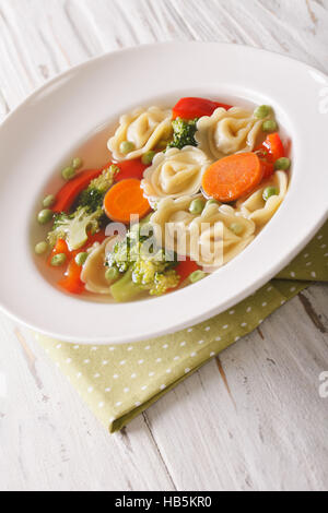 Tortellini-Suppe mit Broccoli, Erbsen, Karotten und Paprika Nahaufnahme auf dem Teller auf den Tisch. vertikale Stockfoto