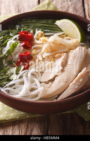 Vietnamesische Küche: Suppe Pho Ga mit Huhn, Reisnudeln und frischen Kräutern in einer Schüssel Nahaufnahme. vertikale Stockfoto