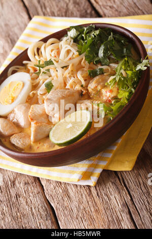 Malaysische Laksa Suppe mit Huhn, Ei, Nudeln und Kräutern hautnah in einer Schüssel auf dem Tisch. vertikale Stockfoto