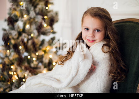 Niedliche kleine Mädchen sitzt durch den Weihnachtsbaum, eingehüllt in eine warme Decke zu Hause Stockfoto