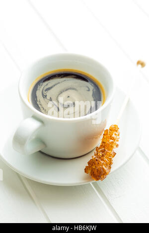Brauner Zucker Bernstein Kristall auf Holzstab und Kaffeetasse auf weißen Tisch. Stockfoto