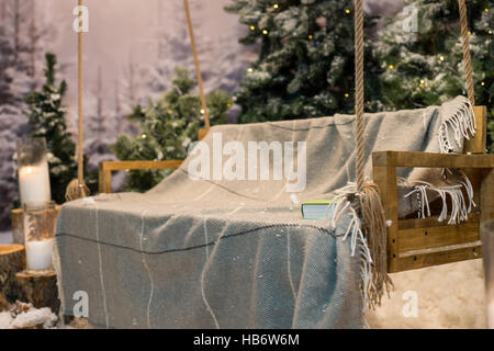 Close up Portrait of Swing mit einer Decke und Buch in einem verschneiten Park oder einen Wald mit Fichten und Baumstümpfe mit großen Kerzen im Glasvasen, Konzept-abo Stockfoto