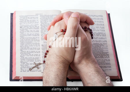 Männliche Hände geschlossen im Gebet Holding einen Rosenkranz über eine alte Bibel. Stockfoto