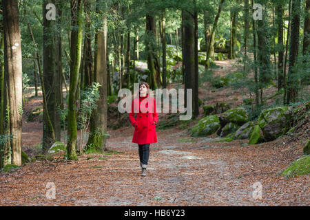 Junge Frau allein zu Fuß auf einem Waldweg Schmutz tragen einen roten Mantel an einem kalten Wintertag Stockfoto