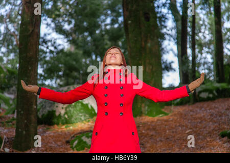 Frau, genießen die Wärme des Sonnenlichts auf einen Wald tragen einen roten langen Mantel winter Stockfoto