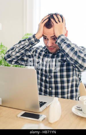 Krank und müde fühlen. Frustrierte junge Mann Kopf in Händen hält, während wir auf Laptop arbeiten im café Stockfoto
