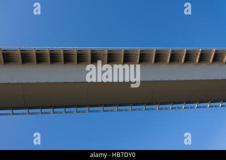 Skurrile aber interessante Aufnahme von der Unterseite eines Teils der Brücke suchen, kantig und moderne vor einem strahlend blauen Himmel Stockfoto