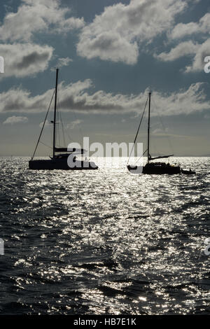 Zwei Yachten in Tenby Bucht früh an einem Sommermorgen verankert. Blauer Himmel mit weißen flauschigen Wolken und die Sonne auf dem Meer reflektiert. Stockfoto