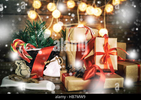 Weihnachtsgeschenke mit Boxen, Nadelholz, Korb, Candy cane Kegel auf hölzernen Hintergrund. Vintage-Stil mit gezeichneten Schneefall Stockfoto