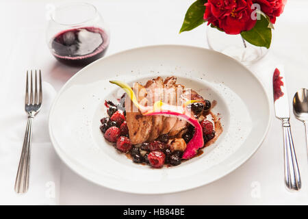 Gebratenes Schweinefleisch mit Beerensauce und einem Glas Pinot Noir Wein Stockfoto