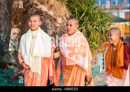 Drei junge weibliche buddhistische Mönche in orangefarbenen Kleidungsstücken ein Spaziergang im Garten Kyaiktiyo-Pagode in Myanmar. Stockfoto