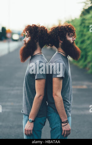 Porträt von identisch Erwachsene männliche Zwillinge mit dem roten Haar und Bärte Rücken an Rücken auf Bürgersteig Stockfoto