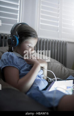 Schulmädchen auf Sofa mit digital-Tablette und Kopfhörer anhören Stockfoto
