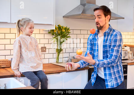 Mitte erwachsenen Mannes jonglieren Obst für Tochter in der Küche Stockfoto