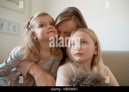Mitte Erwachsene Frau umarmt Töchter im Wohnzimmer Stockfoto