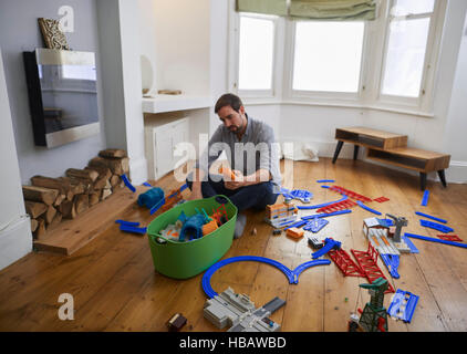 Mitte erwachsenen Mannes verstreut Betrachtung Spielzeug im Wohnzimmer Stockfoto