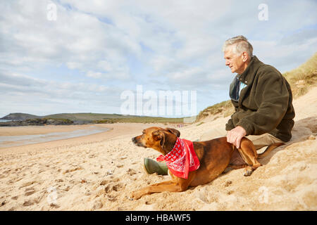 Mensch und Hund sitzen am Strand, Konstantin Bay, Cornwall, UK Stockfoto