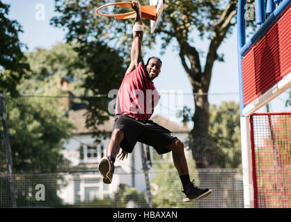 Porträt des jungen männlichen Basketballspieler von Basketballkorb hängen Stockfoto