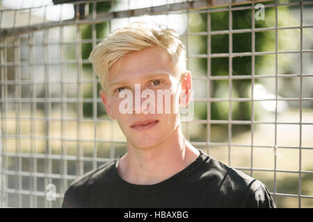 Porträt von blonden Haaren junger Mann Drahtzaun Stockfoto