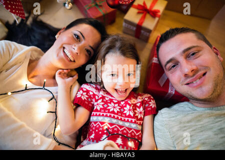 Junge Familie unter dem Weihnachtsbaum unter Geschenke liegen, Stockfoto