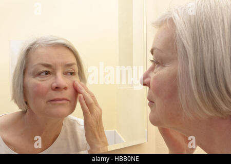 Aging Konzept, ältere Frau, die einen Blick auf die Falten ihrer Gesichtshaut in einem Spiegel, Denken über ästhetische Chirurgie Stockfoto