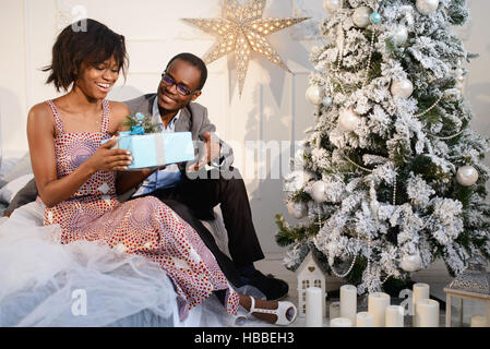 Schönes afroamerikanische Mädchen erhielt ein Geschenk von ihrem Freund am Weihnachtsabend, sie sind auf der Suche im Feld, lächelnd und sehr glücklich Stockfoto