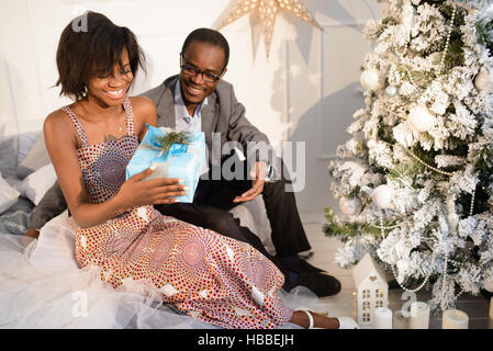 Schöne afroamerikanische Mädchen erhielt ein Geschenk von ihrem Freund auf den Weihnachtsabend, sucht sie in der Box, lächelnd und fühlt sich sehr glücklich Stockfoto