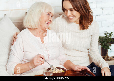 Positive Kranke ältere Frau im Bett zu frühstücken. Stockfoto