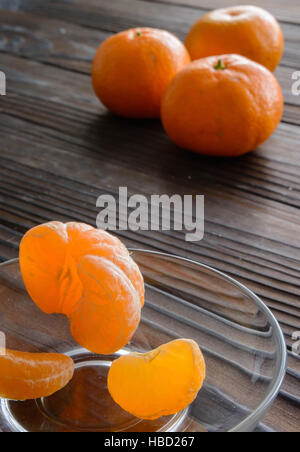 Scheiben von Orange und reifen Mandarine in Glas Untertasse. Vor dem Hintergrund der alten Holztisch. Stockfoto