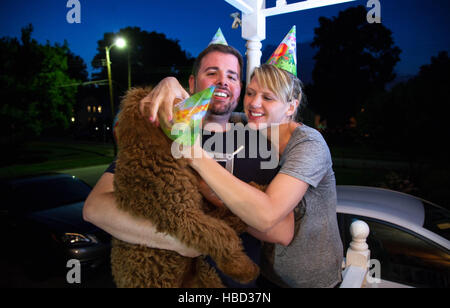 Junges Paar kaukasischen miteinander flirten und Handeln auf einer vorstädtischen Veranda albern halten einen Hund Stockfoto