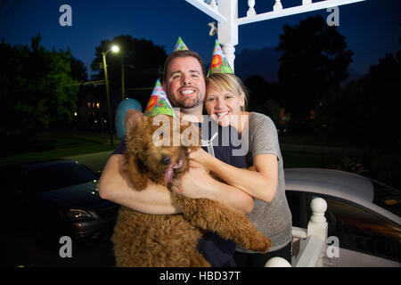 Junges Paar kaukasischen miteinander flirten und Handeln auf einer vorstädtischen Veranda albern halten einen Hund Stockfoto