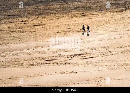 Zwei Personen gesehen, in der Silhouette und aus der Ferne auf dem preisgekrönten Crantock Beach in Newquay, Cornwall. Stockfoto