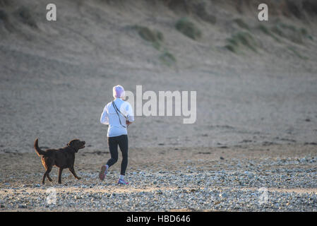 Eine Frau läuft mit ihrem Chocolate Labrador Fistral Strand entlang in Newquay, Cornwall. Stockfoto