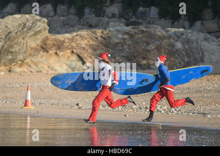 Surfen Sie Santas Rennen am Strand entlang in die jährliche Spendenaktion Santa Surf-Wettbewerb, an einem sehr kalten Fistral Strand in Newquay, Cornwall. VEREINIGTES KÖNIGREICH. Stockfoto