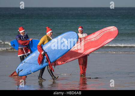 Surfen-Weihnachtsmänner beenden einen Spendenaktionen Santa Surf-Wettbewerb an einem sehr kalten Fistral Strand in Newquay, Cornwall. Stockfoto