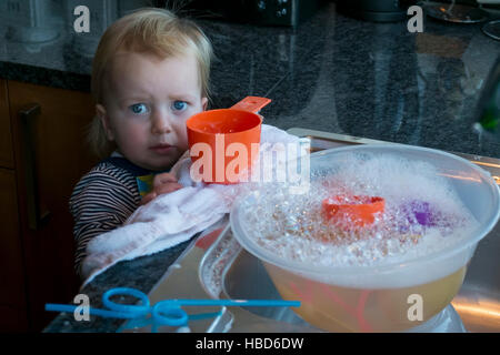 Ein Kleinkind suchen besorgt, als sie mit Luftblasen und Wasser spielt. Stockfoto