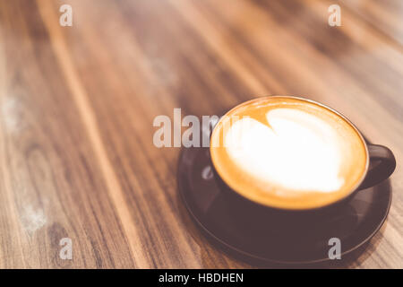 Tasse heißen Cappuccino Kaffee mit herzförmigen Latte Art Schlagsahne Sahne in Vintage-Ton, Textfreiraum auf Holztisch, Liebe oder entspannen Konzept Stockfoto