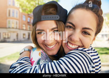 Zwei glückliche junge Mädchen in eine innige Umarmung in die Kamera schaut mit ihren Gesichtern zusammen und strahlendes Lächeln, Nahaufnahme Kopf und Schultern Stockfoto