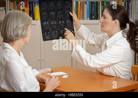 2 Frauen in einer Operation: mittlere gealterte Arzt in Laborkittel zeigen ihre älteren Patienten Magnetresonanz-Bilder ihres Kopfes Stockfoto