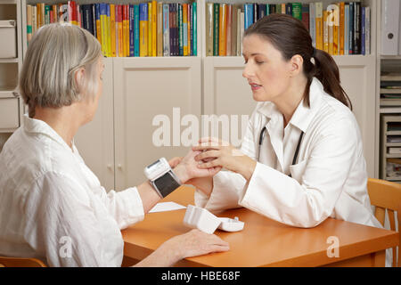 Applying Arzt, ihr senior Patientin zu erklären, die korrekte Verwendung von einem Handgelenk-Blutdruckmessgerät Stockfoto