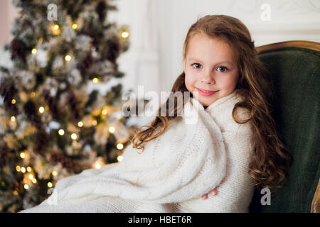 Niedliche kleine Mädchen sitzt durch den Weihnachtsbaum, eingehüllt in eine warme Decke zu Hause Stockfoto