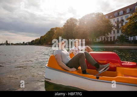 Aufnahme von zwei jungen Freunden sitzen im Tretboot und Pedale. Jungs im Teenageralter Bootfahren auf dem See in der Stadt. Stockfoto