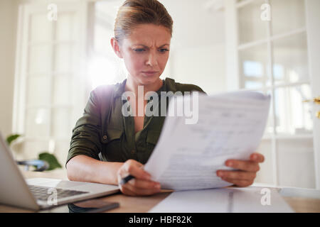 Porträt des jungen weiblichen sitzen am Tisch, die Dokumente zu lesen. Frau fleißig zu Hause Büro. Stockfoto
