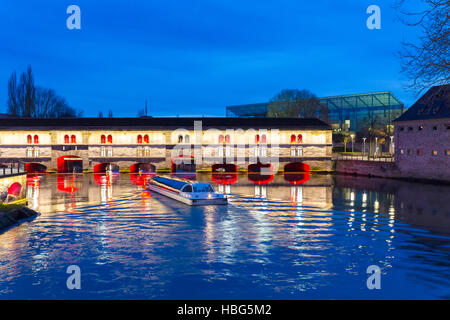 Ausflugsschiff mit Touristen vor der Barrage Vauban (Vauban-Wehr) nachts entlang dem Fluss Ill, Straßburg, Frankreich Stockfoto