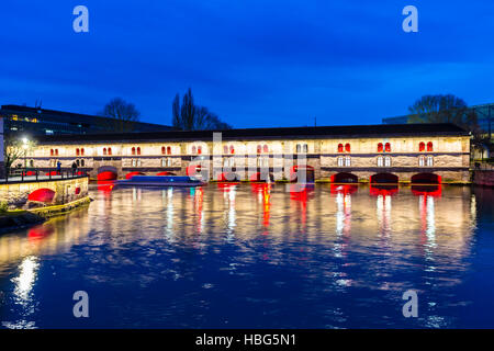 Ausflugsschiff mit Touristen vor der Barrage Vauban (Vauban-Wehr) nachts entlang dem Fluss Ill, Straßburg, Frankreich Stockfoto