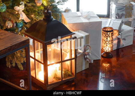 Nahaufnahme der Geschenke unter dem Weihnachtsbaum und Kerze in einer Lampe Stockfoto
