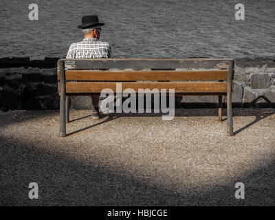 Alter Mann sitzt auf einer Holzbank Stockfoto