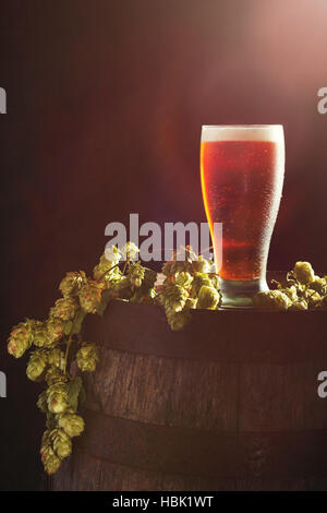 Pint Bier in einem Glas auf ein Holzfass mit Hopfen Stockfoto