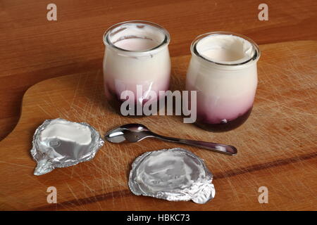 Joghurt mit Marmelade in offenen kleinen Glas mit Löffel auf Holzbrett Stockfoto