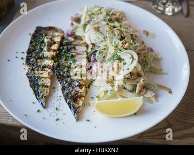 Makrele Fischfilets serviert mit einem Salat mit Apfel und Walnüssen. Auf einem weißen Teller auf einem Holztisch mit einer Scheibe Zitrone. Stockfoto